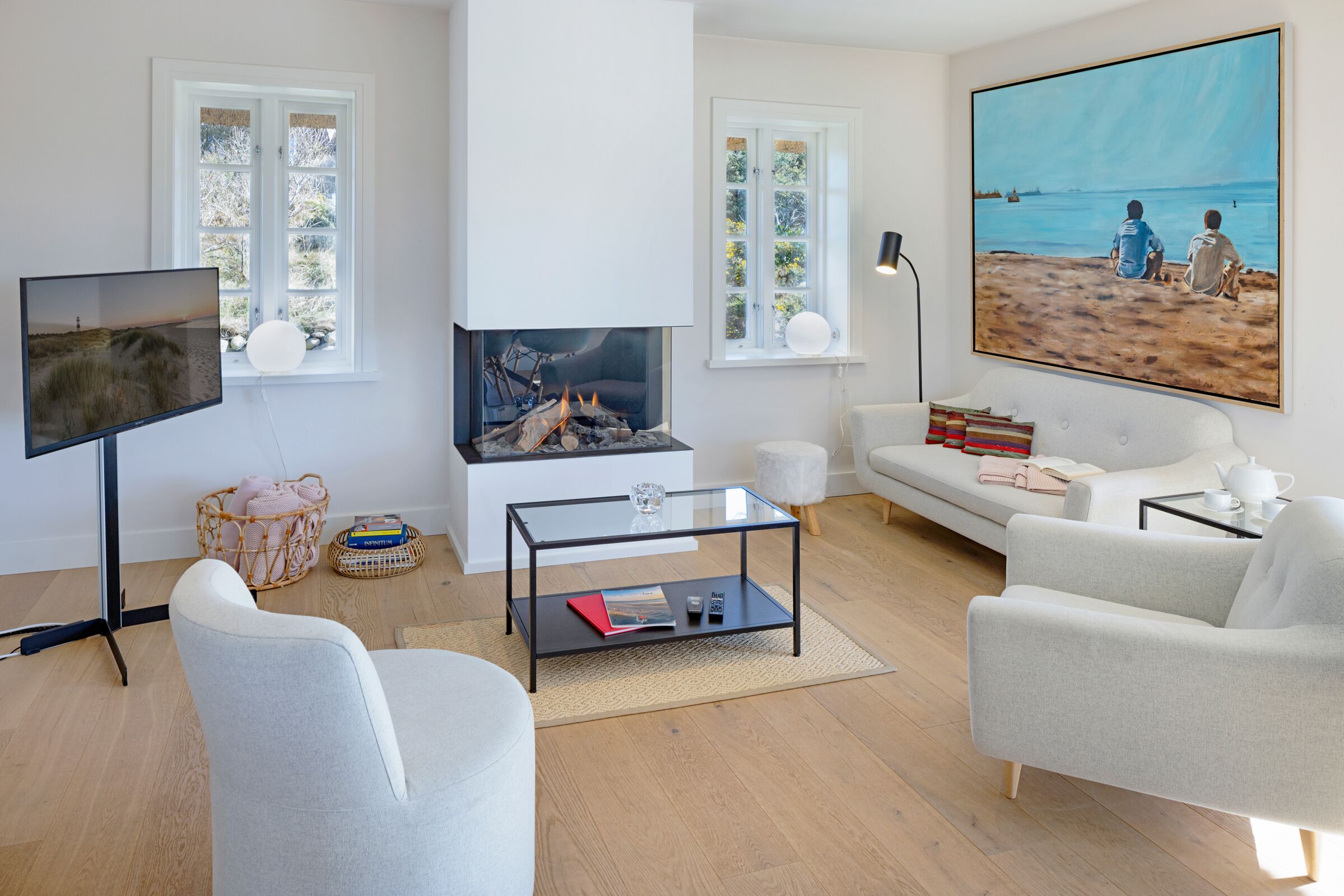 Una sala de estar moderna con chimenea, asientos cómodos, un televisor de pantalla plana y un cuadro grande de playa.
