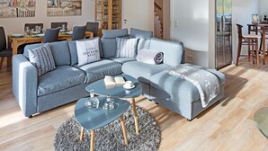 Ein modernes Wohnzimmer mit einer Eckcouch, einem Glastisch und einem Essbereich mit einem Holztisch und Stühlen.
