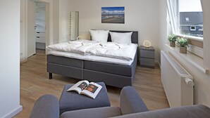 Ein modernes Schlafzimmer mit einem großen Bett, Nachttischen, einem Fenster mit Pflanzen und Blick ins Freie.