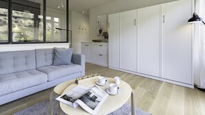 A modern living room with a grey sofa, a round coffee table with a magazine, and white cabinets in the background. - Herzlich Willkommen im Appartement Heideblick (List)