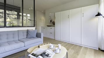 Een moderne woonkamer met een grijze bank, een ronde salontafel met een tijdschrift en witte kasten op de achtergrond.