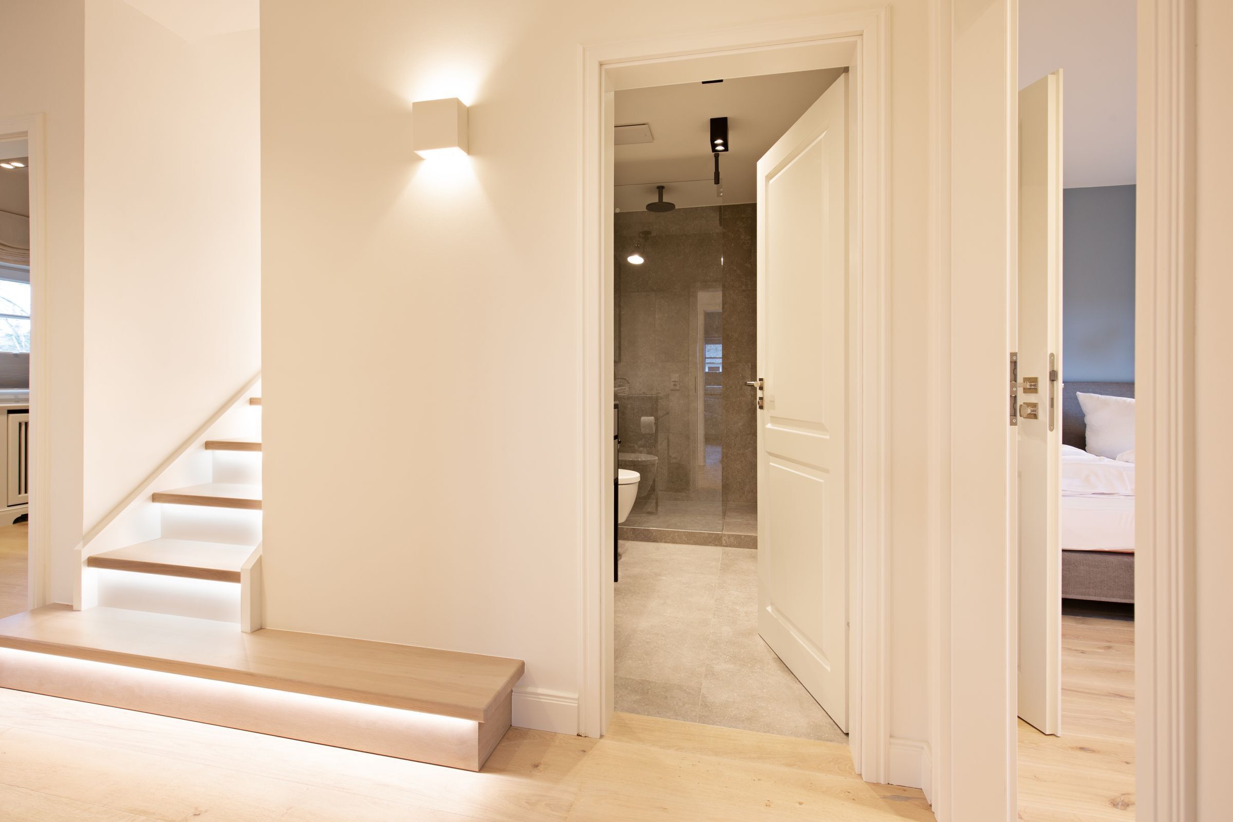Ein modernes Interieur mit einer Treppe zu einem Badezimmer, einem sichtbaren Duschbereich und einem Schlafzimmer mit einem Bett.