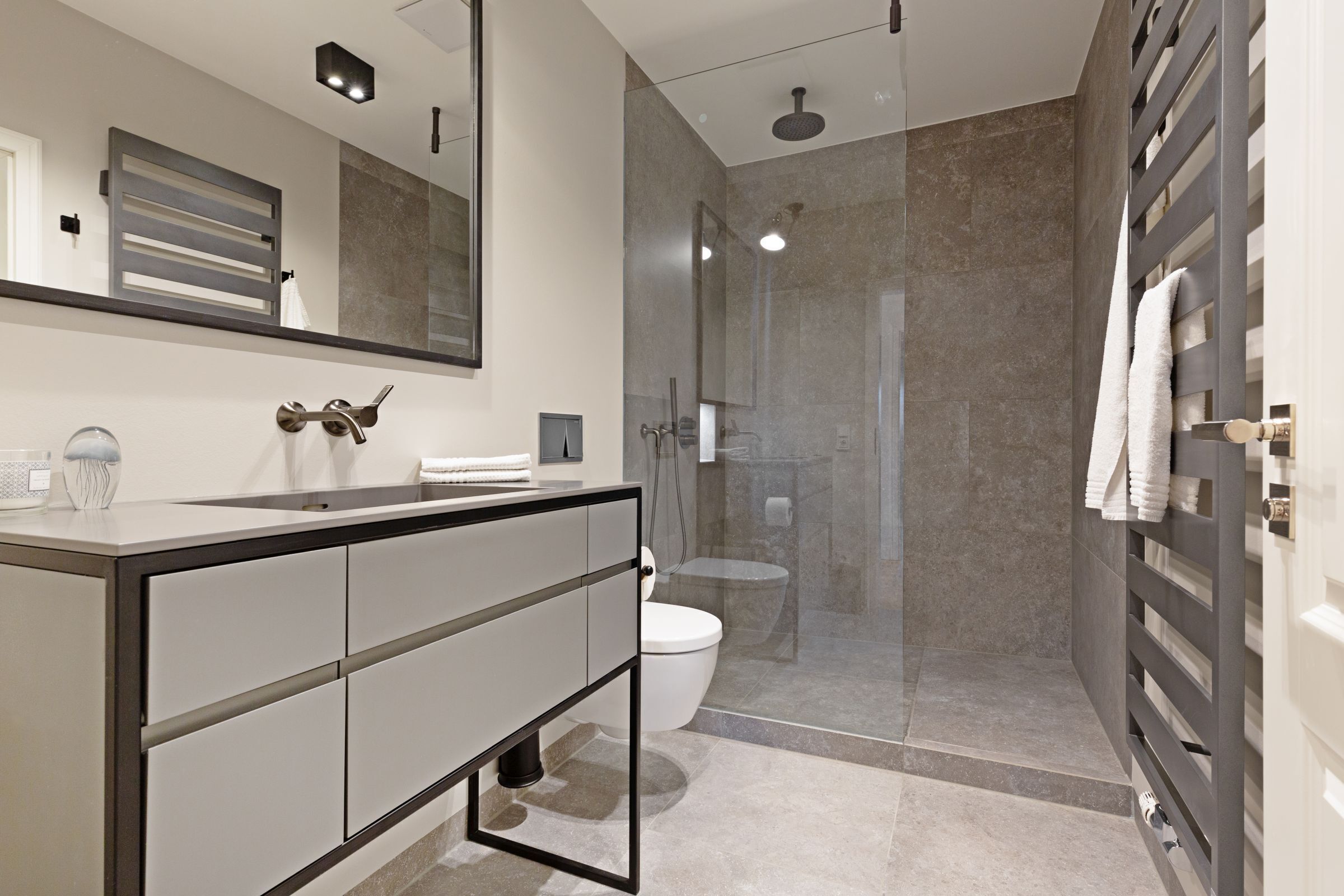 A modern bathroom with a glass-enclosed shower, a white toilet, and a vanity with a mirror and towel rack.