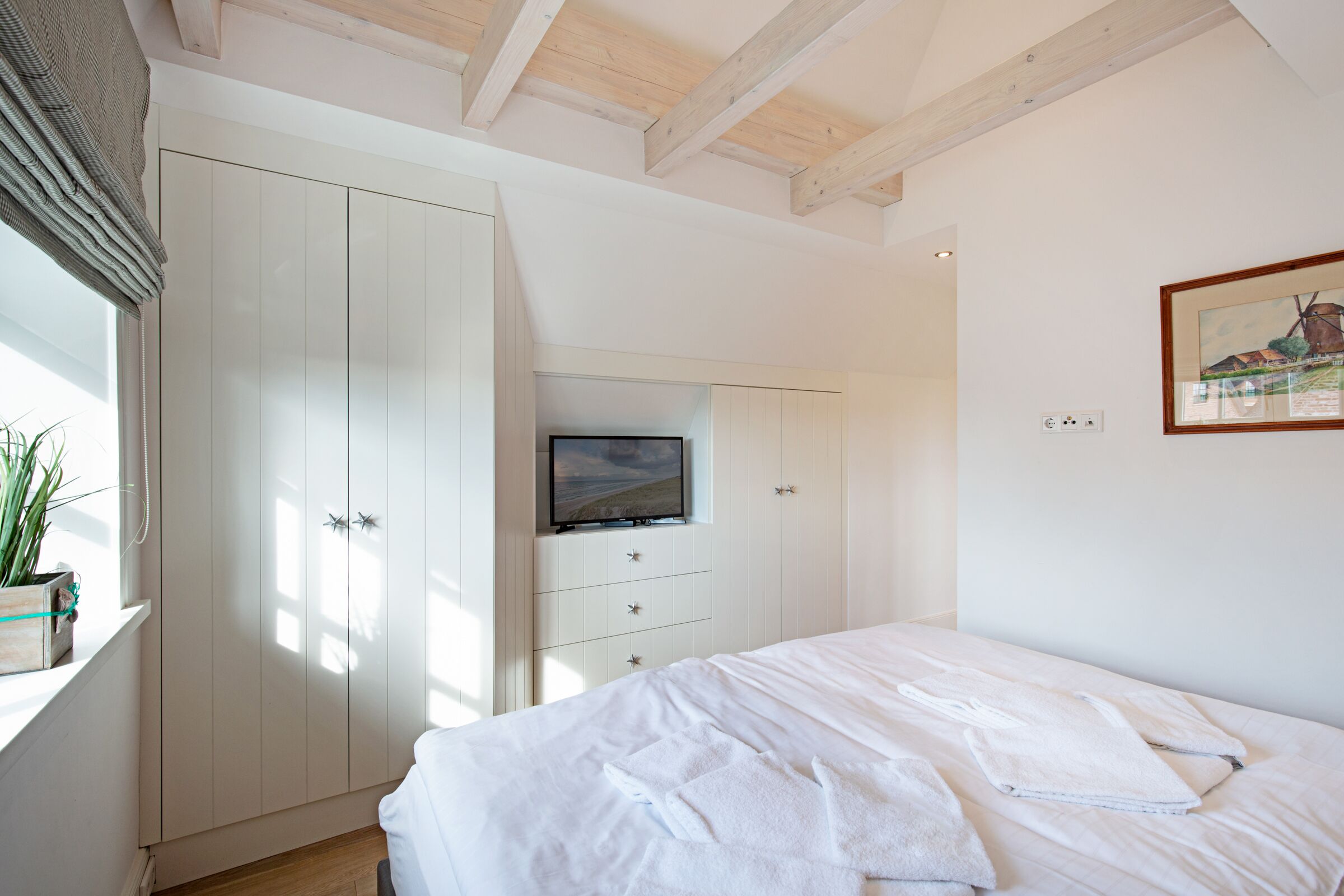 A bedroom with a bed, a wardrobe, a television, and a painting on the wall.