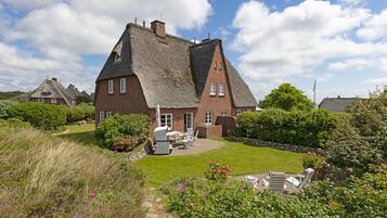 A large brick house with a thatched roof, a well-maintained lawn, and outdoor seating area.