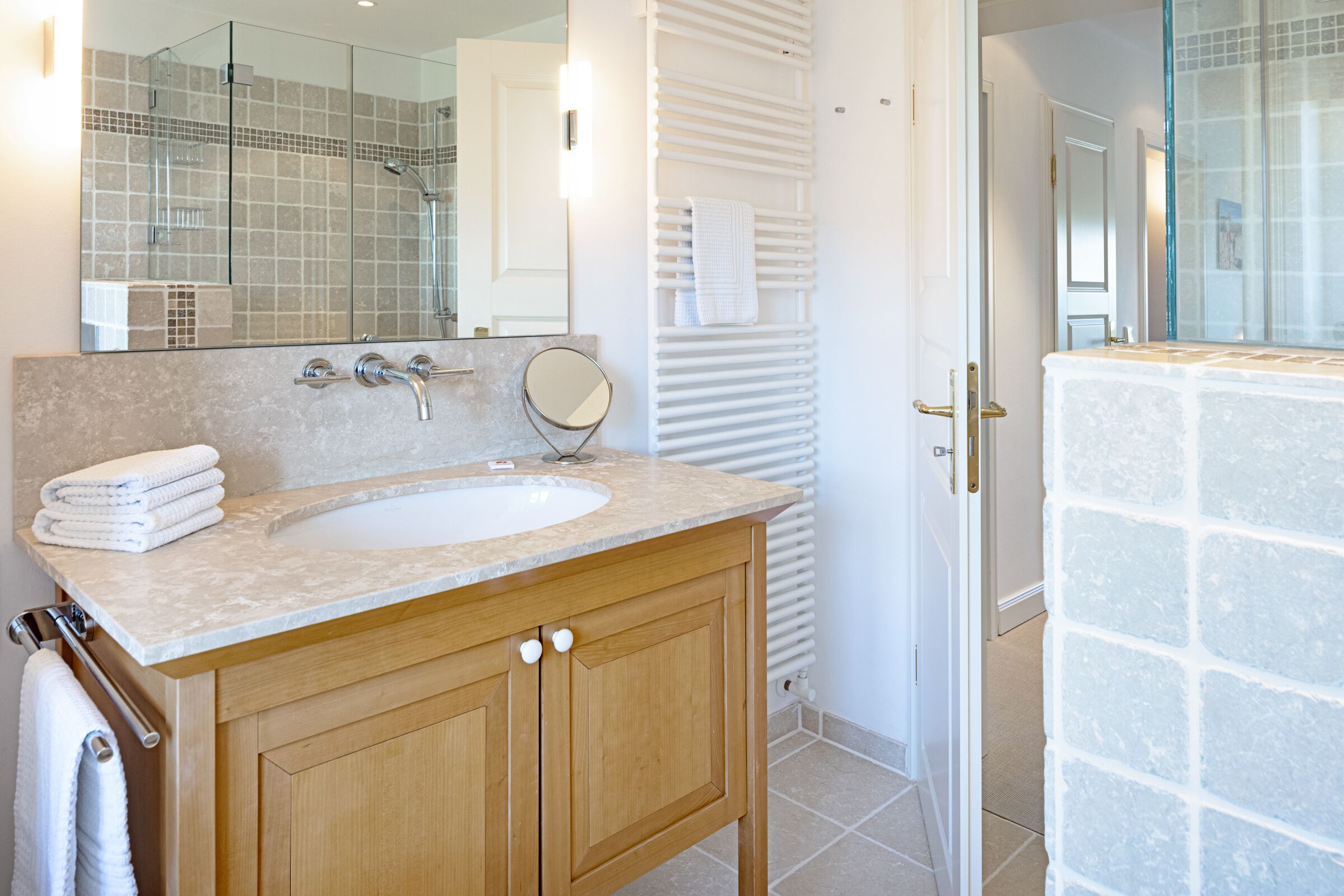 Un baño con tocador de madera, un lavabo, un espejo y mampara de vidrio para la ducha.