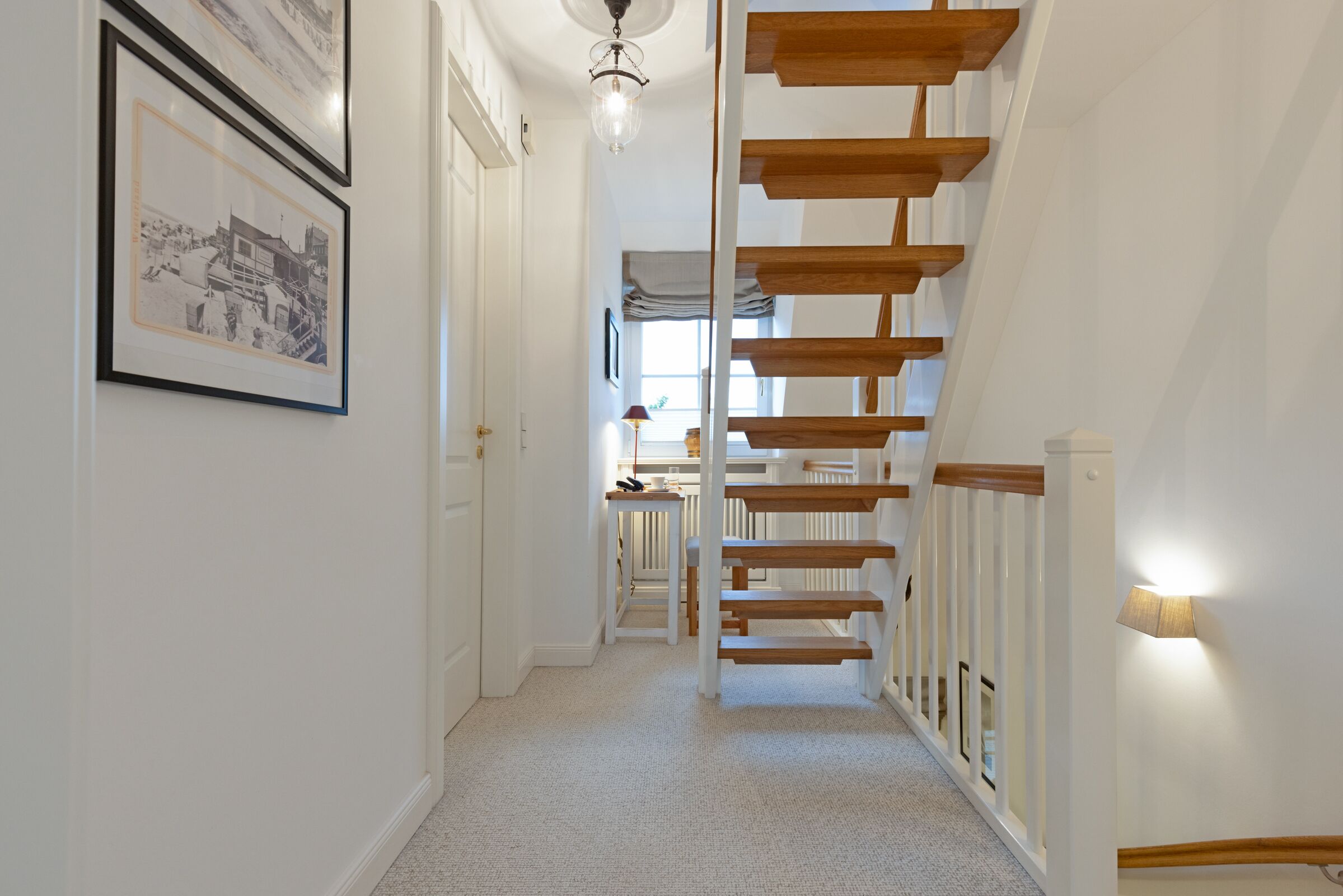 A hallway with a wooden staircase, white walls, and a framed picture on the left.