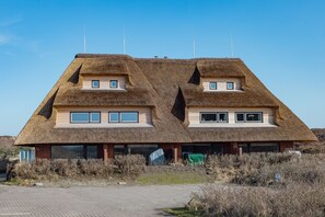 Un bâtiment doté d’une toiture en chaume au design unique, comprenant deux parties principales avec de petites fenêtres et une cheminée centrale.