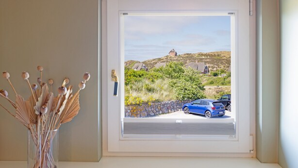 A window with a clear view of a street, cars, and a building on a hill.