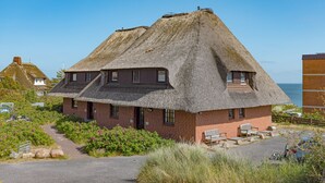 A thatched-roof house with a brick exterior, a small porch with seating, and a view of the sea.