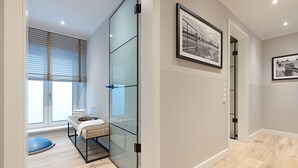 Une pièce moderne avec une cloison en verre, un banc, une petite table avec des serviettes et des tableaux encadrés au mur.