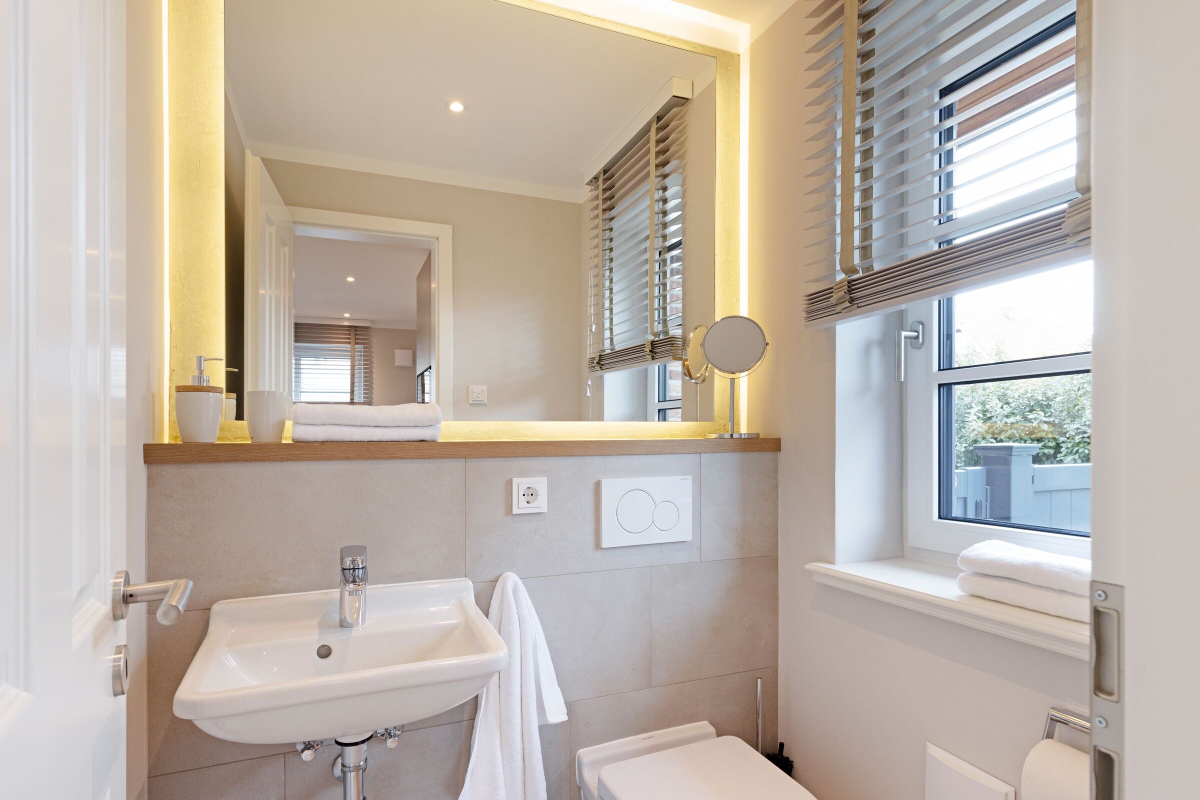 A modern bathroom with a sink, mirror, window with blinds, and a towel rack.