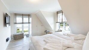 Une chambre avec un grand lit, une petite table et une fenêtre avec des stores.