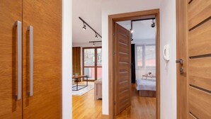 A modern interior with wooden flooring, a bed with a white headboard, and a small table with a chair. - Industrial Apartment Fredry with Parking by Noclegi Renters (Kraków)
