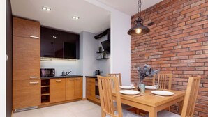 A modern kitchen with wooden cabinets, a brick wall, and a dining table set for four. - Industrial Apartment Fredry with Parking by Noclegi Renters (Kraków)