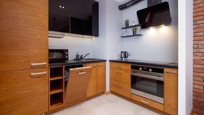 A modern kitchen with wooden cabinets, a black countertop, a built-in oven, and a wall-mounted shelf with plants. - Industrial Apartment Fredry with Parking by Noclegi Renters (Kraków)