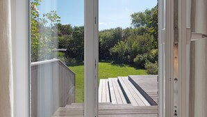 An open door leading to a wooden deck with a view of a garden and trees.