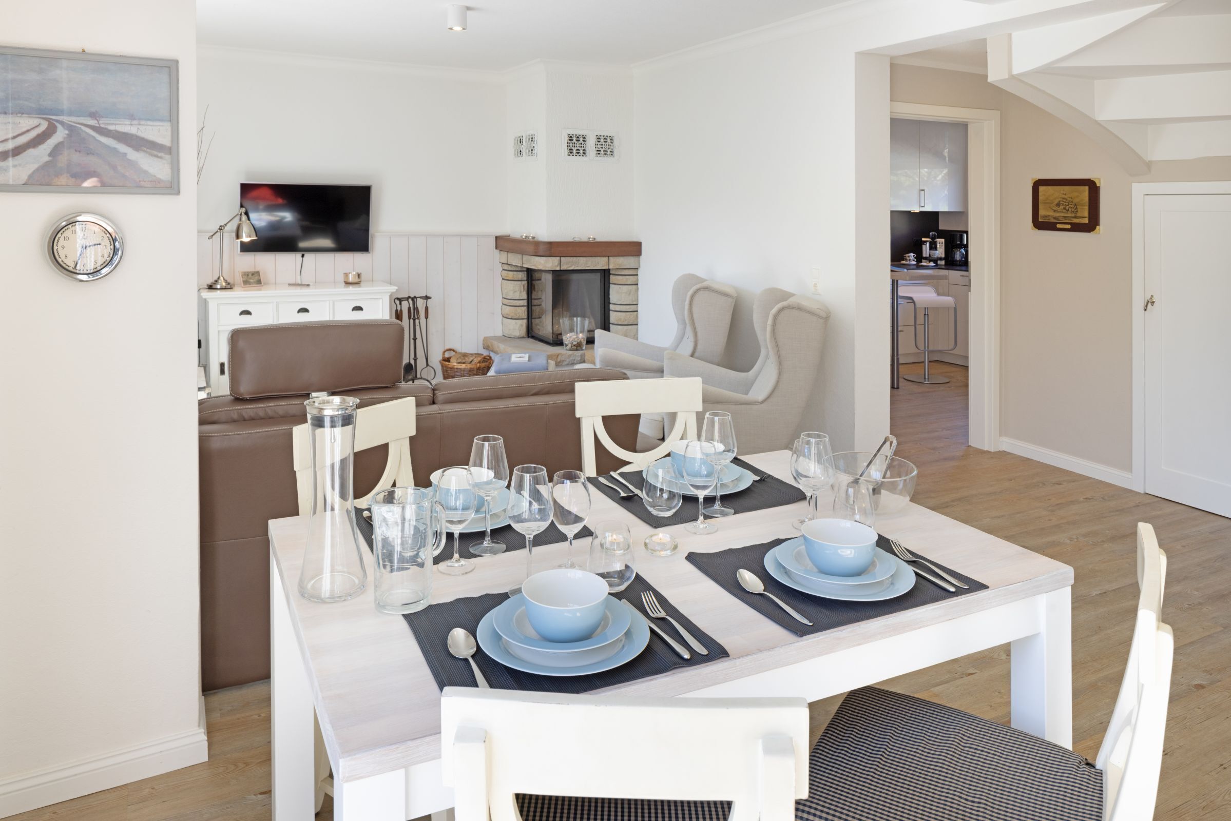 A dining area with a table set for four, a sofa, a television, and a kitchen in the background.