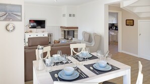 A dining area with a table set for four, a sofa, a television, and a kitchen in the background.