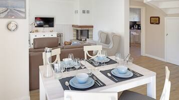 A dining area with a table set for four, a sofa, a television, and a kitchen in the background.