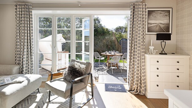 Una habitación luminosa con sofá, sillón, mesa de comedor y vistas a un patio exterior a través de un ventanal.