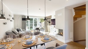 Un comedor moderno con una mesa de madera dispuesta para seis personas, una chimenea y una escalera que sube a un nivel superior.
