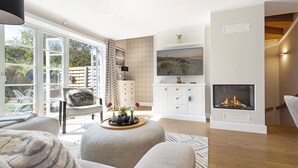 Una sala de estar moderna con chimenea, un televisor montado en la pared y un amplio ventanal con vistas al exterior.