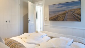 Un dormitorio con una cama, almohadas, una almohada a rayas, una puerta de madera y un cuadro con una escena de playa.