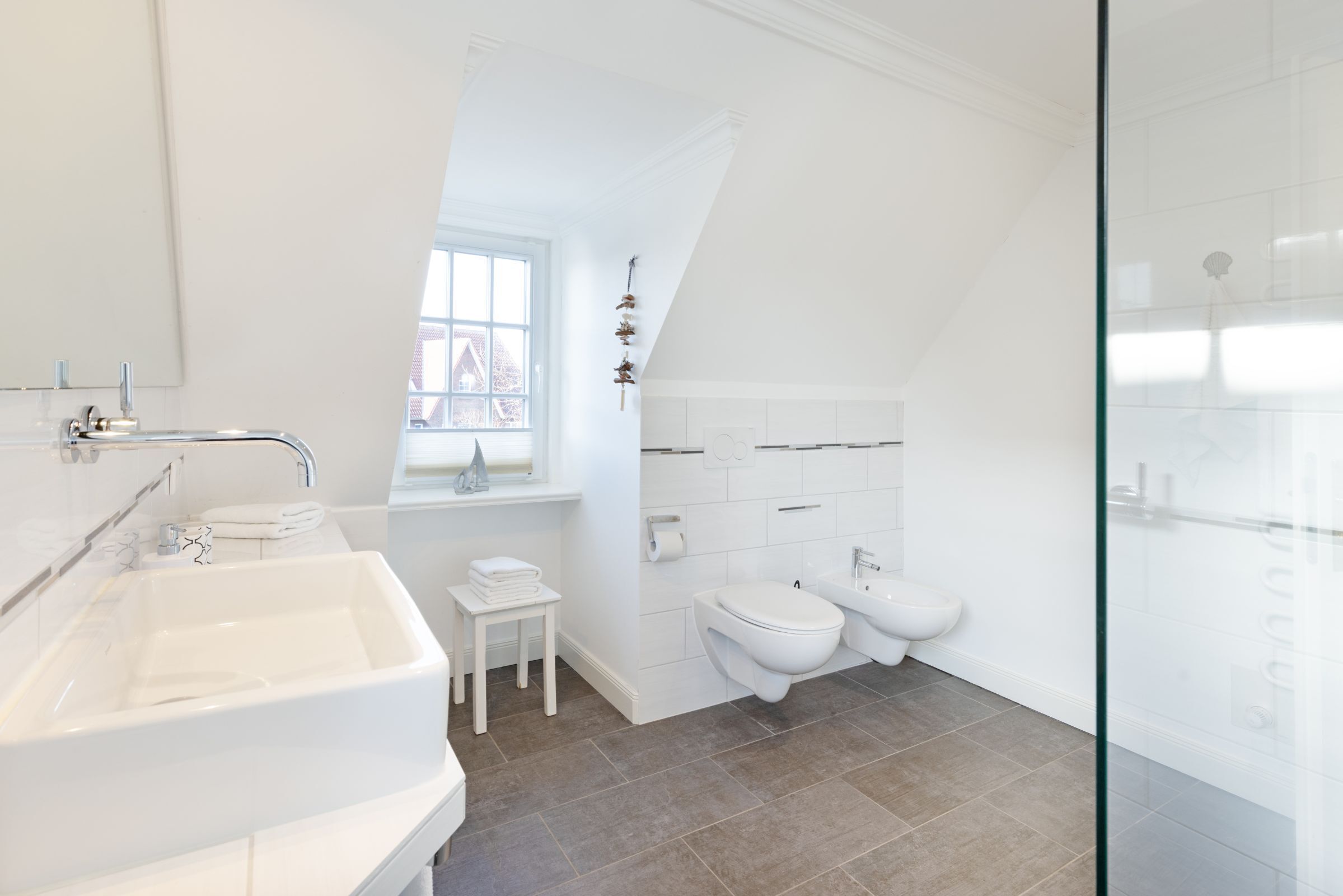 Ein modernes Badezimmer mit einem großen Waschbecken, Toilette, Bidet und einer Duschkabine aus Glas.