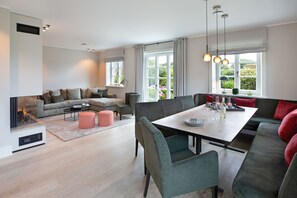 A modern living room with a fireplace, a dining area with a table set for four, and a large window with curtains.