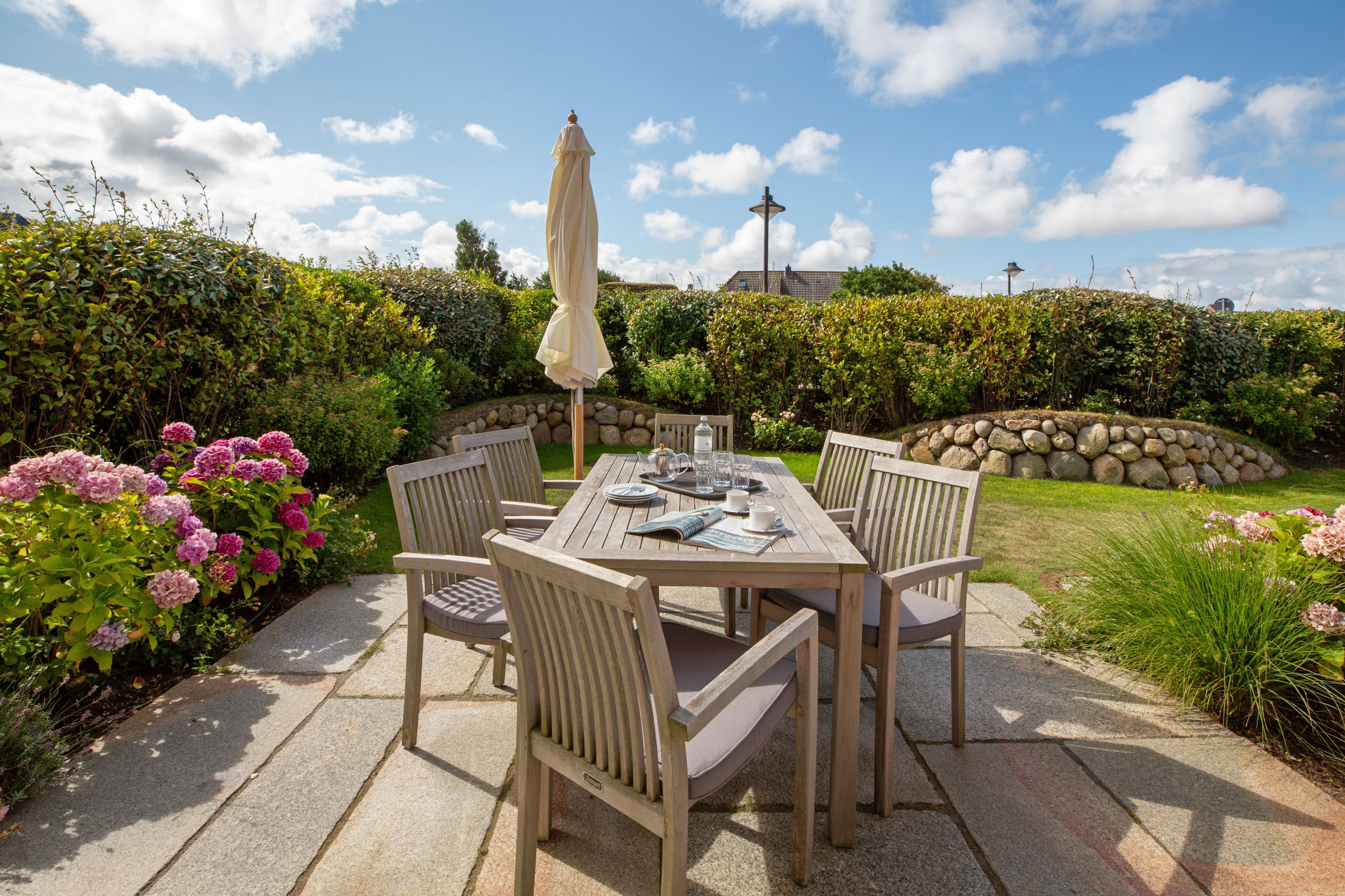 An outdoor patio with a wooden table and chairs, a table umbrella, and a stone wall in the background.