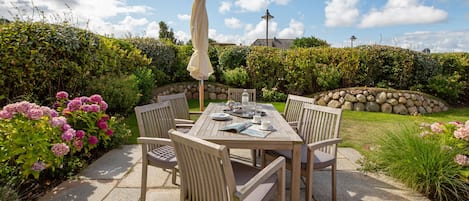 An outdoor patio with a wooden table and chairs, a table umbrella, and a stone wall in the background.