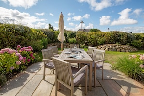 An outdoor patio with a wooden table and chairs, a table umbrella, and a stone wall in the background.