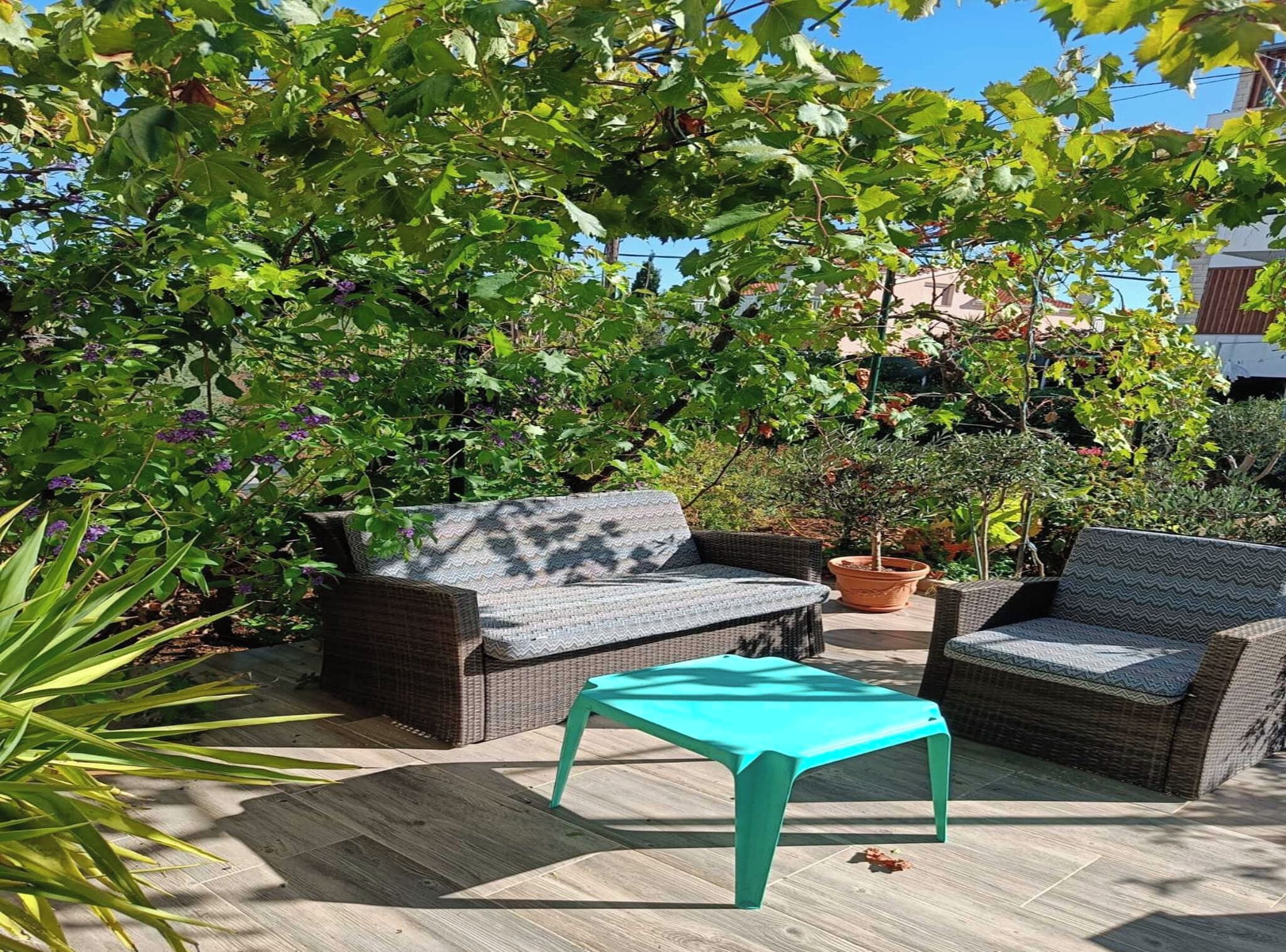 Un espace extérieur aménagé avec des meubles en osier et une table turquoise, entouré d’une végétation luxuriante et sous un ciel dégagé.