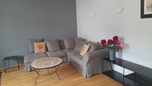 Un salon moderne avec un canapé d’angle gris, une petite table ronde et un vase de fleurs.