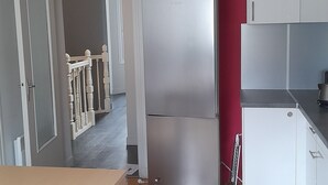 Une cuisine équipée d’un réfrigérateur, de placards, d’un luminaire suspendu et d’un plancher en bois.