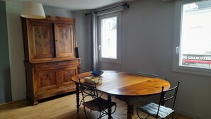 Un coin repas comprenant une table en bois, des chaises, un buffet et une fenêtre donnant sur la rue.