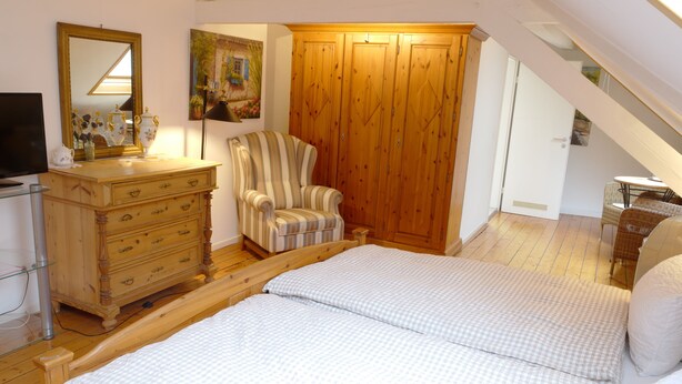 A bedroom with a wooden bed, a dresser, a chair, a wardrobe, and a television. - Landgasthof Kirschgarten (Ingelheim am Rhein)