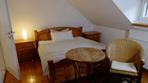 A bedroom with a wooden bed, a bedside table with a lamp, a wicker chair, and a patterned rug. - Landgasthof Kirschgarten (Ingelheim am Rhein)