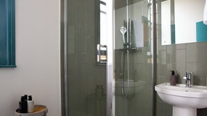 A modern bathroom with a glass-enclosed shower, a white sink, and a small vanity with toiletries. - The Crown Rooms (London)