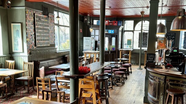 A spacious restaurant with wooden tables and chairs, a bar area, and large windows allowing natural light. - The Crown Rooms (London)