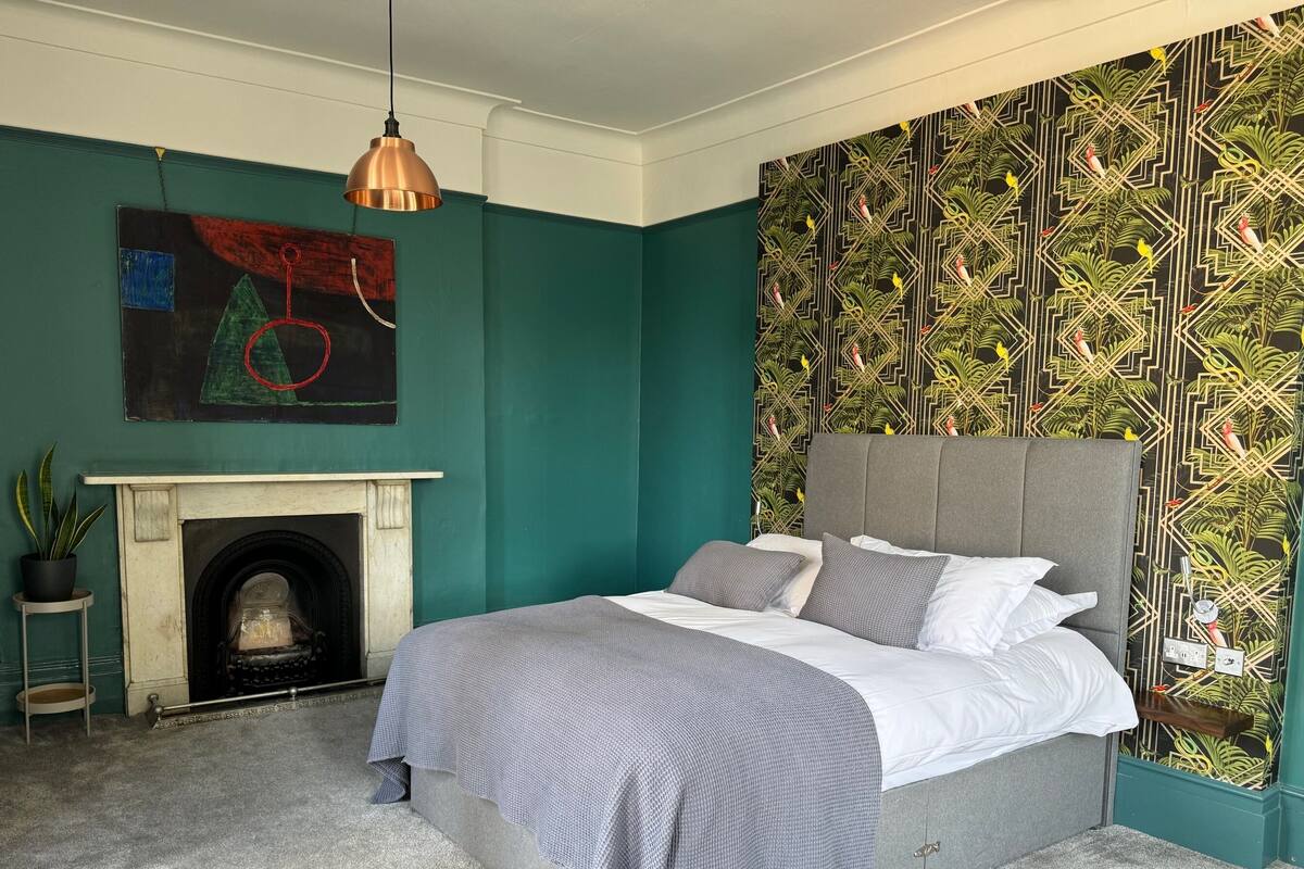 A bedroom with a bed, a fireplace, and a patterned wallpaper.
