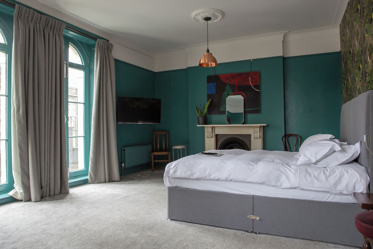 A bedroom with a bed, a fireplace, a television, and large windows with curtains.