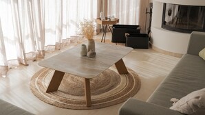 Uma sala de estar moderna com um sofá claro, um tapete redondo de fibra natural, uma mesa de centro de madeira com um vaso e uma lareira.