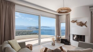 Uma sala de estar moderna com uma grande janela que oferece uma vista panorâmica do mar e das montanhas.