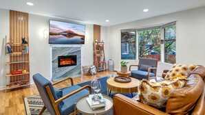 Un salon moderne doté d’une cheminée, de sièges confortables, d’un grand téléviseur et offrant une vue sur l’extérieur.