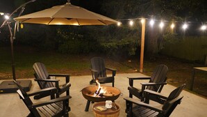 Une terrasse extérieure avec quatre fauteuils Adirondack, un foyer et un parasol pour faire de l’ombre.