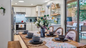 Une cuisine moderne avec des meubles blancs, un four encastré et un coin repas doté d’une table en bois, mise pour six personnes.