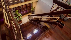 A wooden staircase with a handrail, leading to a lower level. There are potted plants on the landing and a decorative wall with lights. - Baan Kong Hostel (Takua Pa)