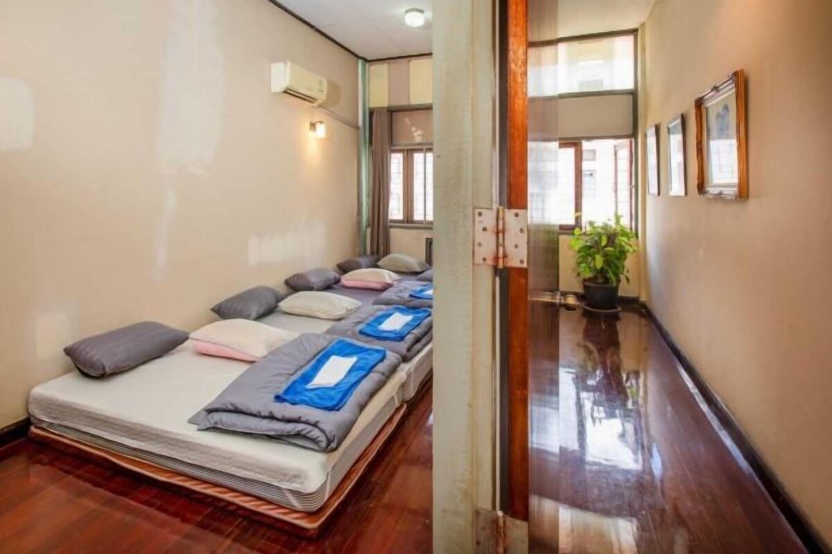Habitación de hotel con cama, almohadas, una planta en maceta y un pasillo con espejo y cuadros enmarcados.